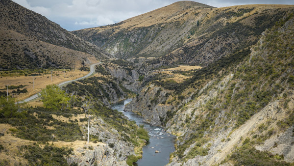 River in a gorge with a road and patchy dry vegetation beside it.