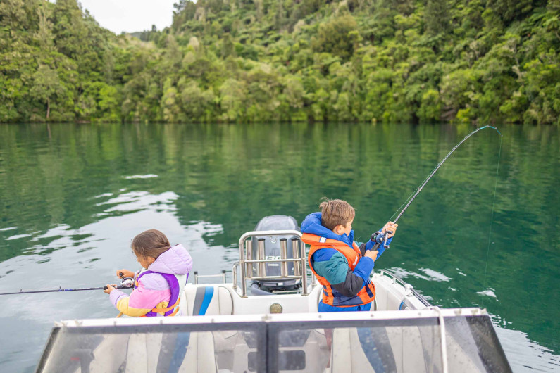 Two children fishing off the back of a boat on a lake