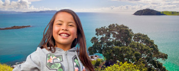 A girl smiles in the foreground with a view of the bay behind. 