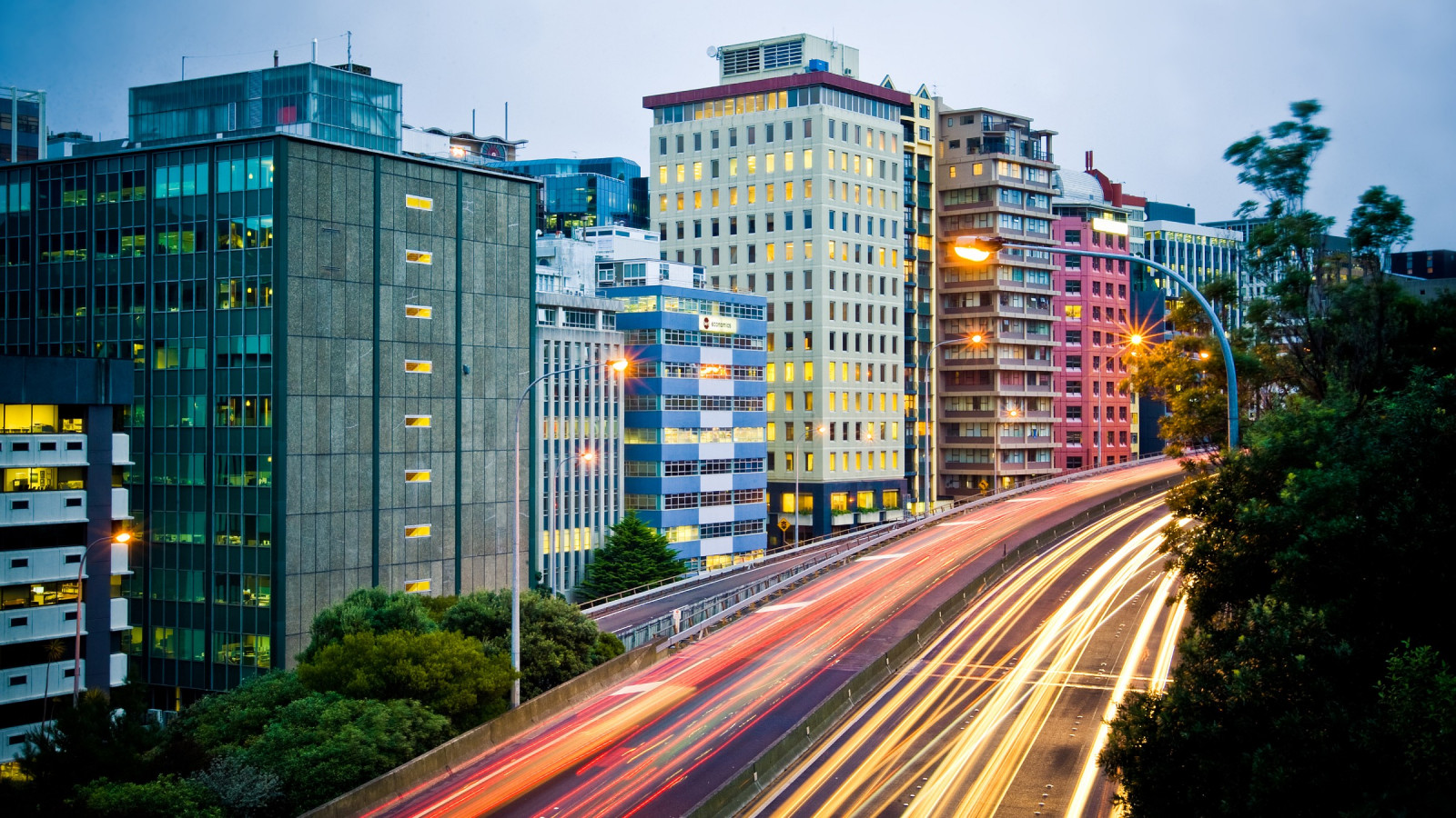 Cityscape with a highway in the foreground surrounded by trees. 