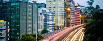 Cityscape with a highway in the foreground surrounded by trees. 