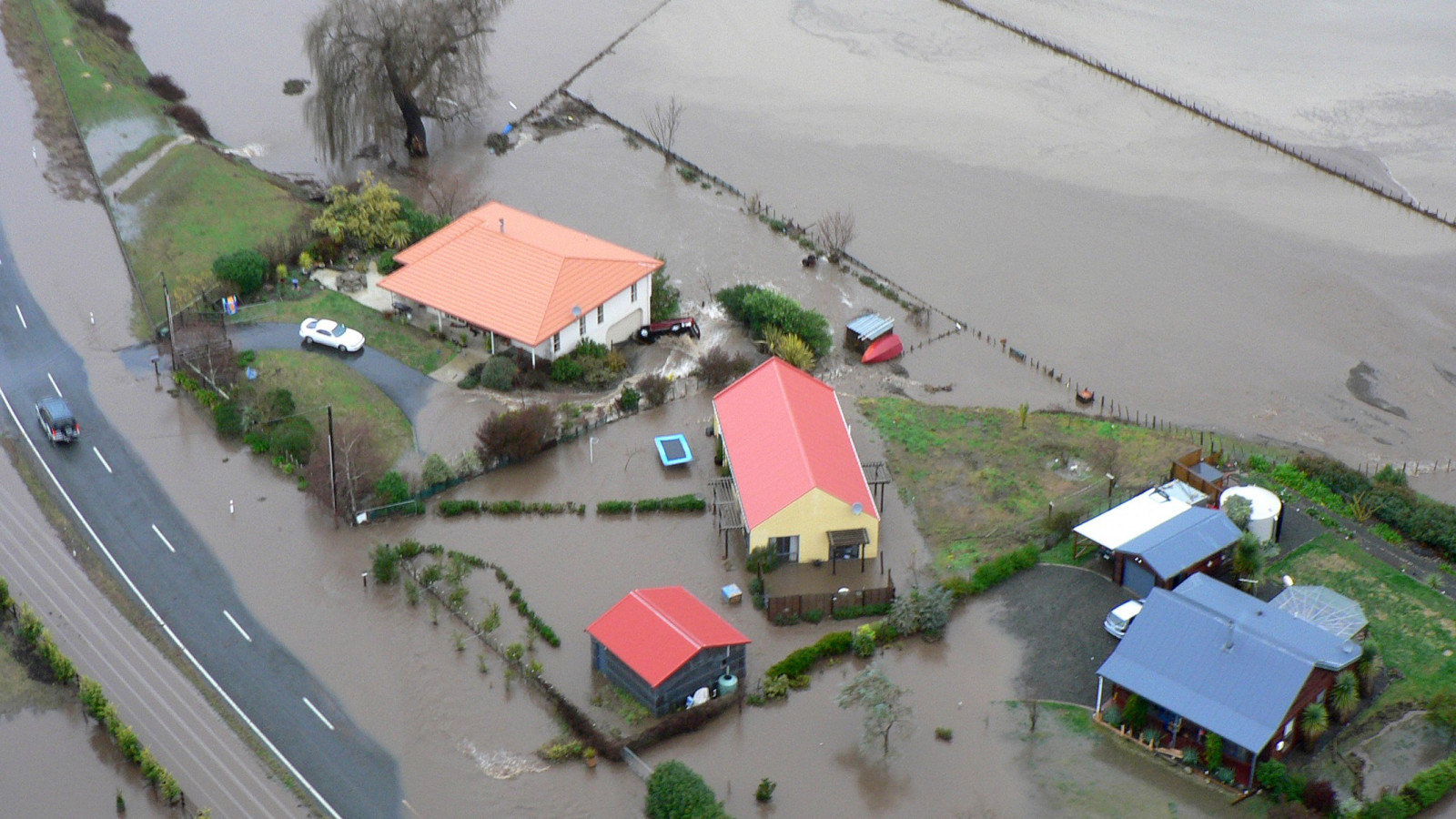 Brown floodwater reaches up to five houses and covers a road and large paddocks.