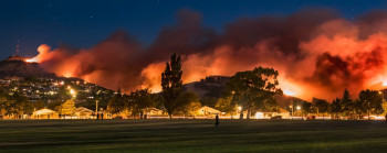 A large wildfire at night, with red smoke above the hills.