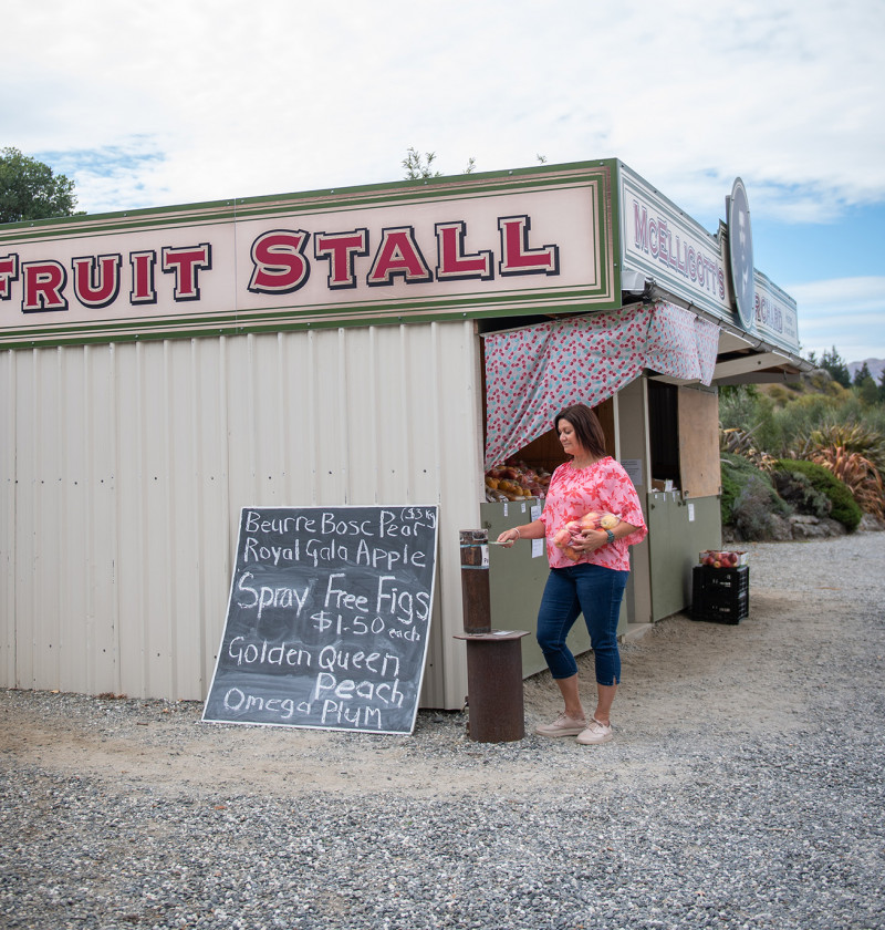 A woman purchasing a bag of apples from a roadside fruit stall. 