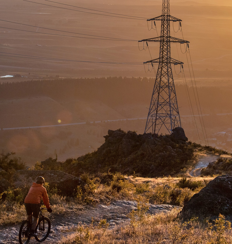 A person mountain biking at sunrise. A large electricity pylon with wires is at the centre of the image.