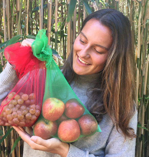 A woman holding two reusable produce bags with fruit in them.