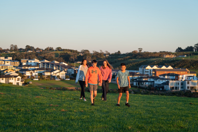 Four young people walking in a field. Houses are visible in the background.