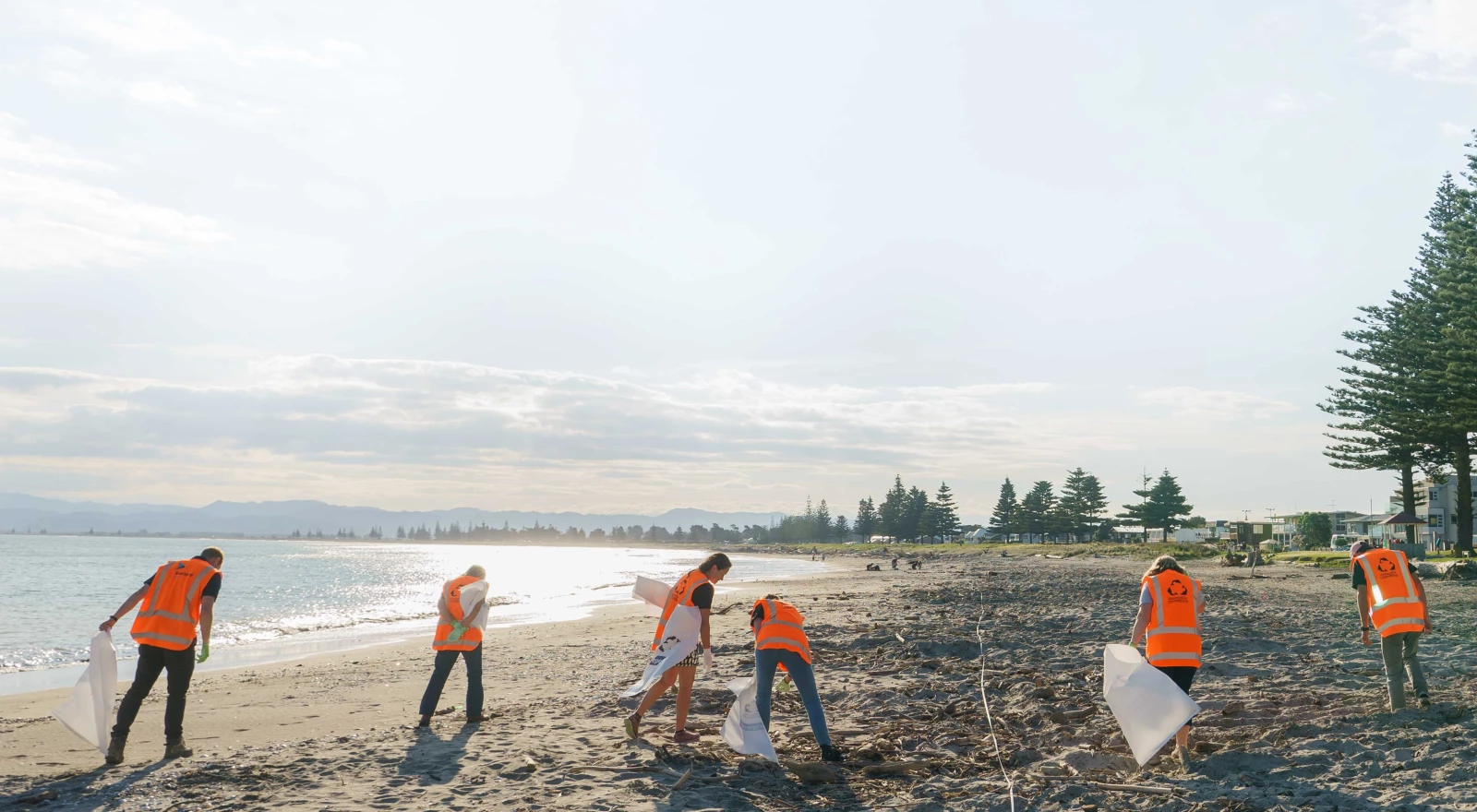 A group of people in hi-vis vests and rubbish bags, picking up rubbish along a beach.