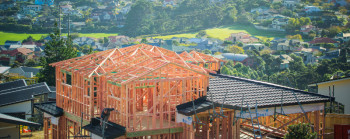 The framing of a new two-story house, with other suburban houses in the background. 