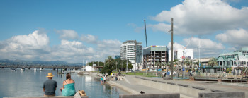 Two adults sitting by a harbour showing the ocean and city buildings. 