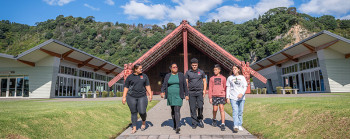 A group of people walking along a path in front of a marae.  