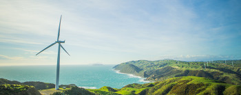 A wind turbine on farmland with the ocean in the background.  