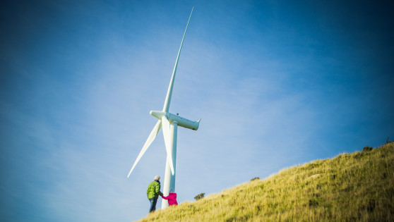 Two people stand by a wind turbine on a hill.  