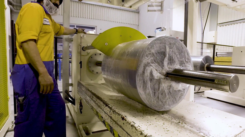 A man in a jumpsuit in front of a machine part of a plastic recycling and manufacturing facility.